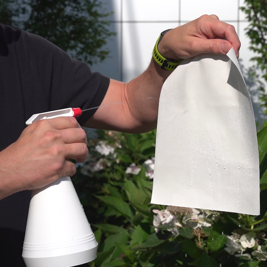 Eine Person sprüht mit einer Sprühflasche Wasser auf ein Stück Stoff, das Wasser perlt ab.