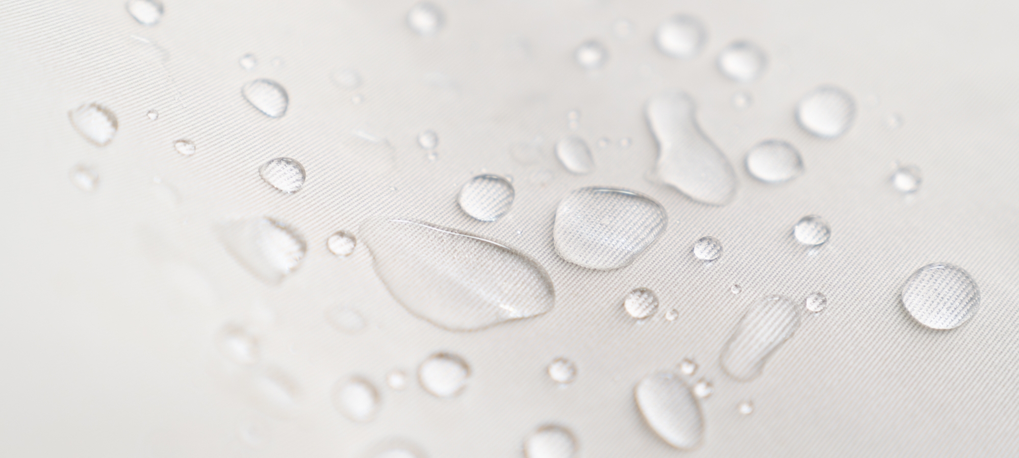 Wassertropfen perlen von einem hellen, beschichteten Stoff ab