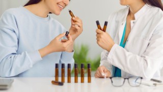 two women sitting at lab table with little brown glass rollerball bottles and smelling various essential oils or different perfume samples. 